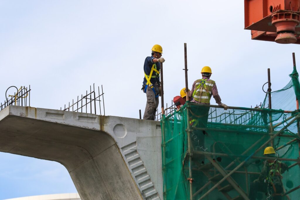 3 men in yellow hard hat and yellow hard hat standing on green metal frame during